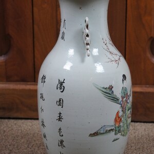 Op de afbeelding: Een witte porseleinen vaas met twee handvatten en een bloemenmotief. De vaas heeft Chinese karakters aan de zijkant, waaronder "Qing-dynastie" en "Gemaakt in China".