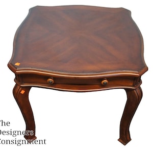 May include: A dark brown wooden end table with a single drawer and curved legs. The table top has a wood grain pattern.