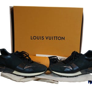 May include: A pair of black leather sneakers with white soles and a silver accent. The sneakers are in a box with the Louis Vuitton logo.