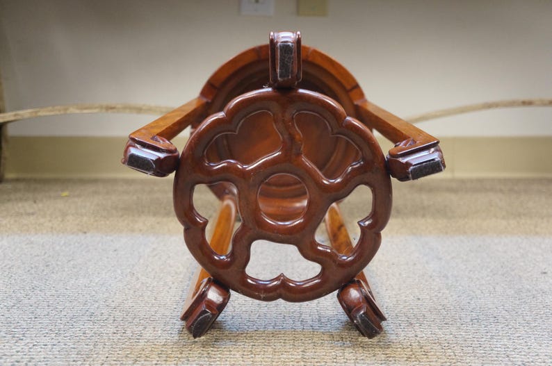May include: A dark brown wooden stool with a decorative, openwork design on the seat and legs. The stool has a glossy finish and appears to be made of a hardwood. The design is reminiscent of Asian furniture.