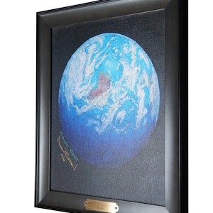 May include: A framed painting of a blue and white Earth with a black background. The painting is signed "Alan Bean" and "Apollo XII" in gold lettering. The frame is black wood with a gold plaque that reads "Mission to the Planets".