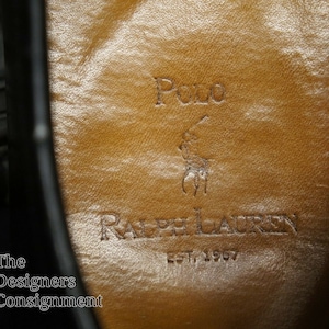 May include: Close-up of the inside of a black leather shoe with a brown leather insole. The insole has the Polo Ralph Lauren logo and the text "EST. 1967".