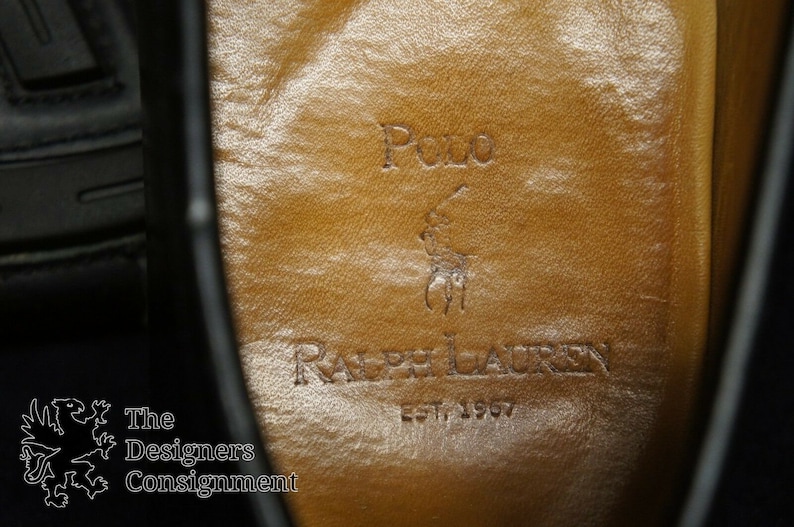May include: Close-up of the inside of a black leather shoe with a brown leather insole. The insole has the Polo Ralph Lauren logo and the text "EST. 1967".