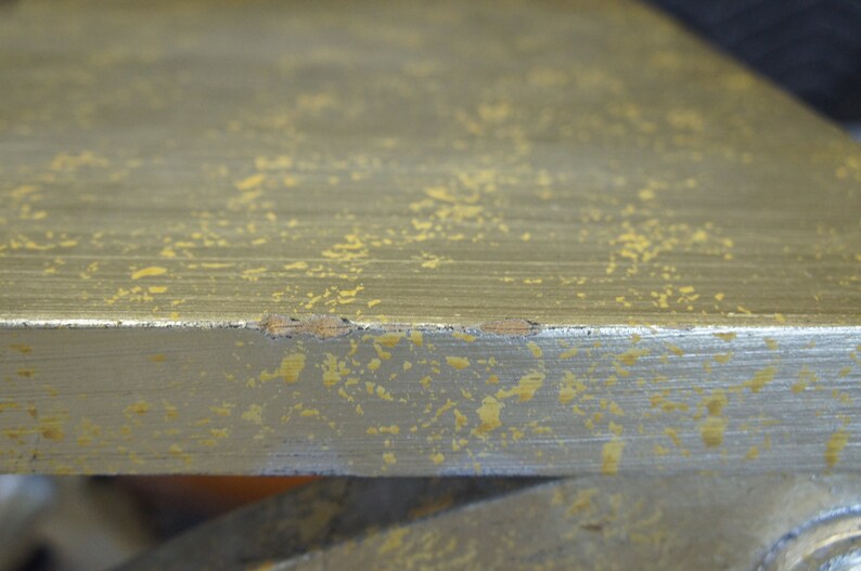 K&ouml;nnte beinhalten: Nahaufnahme einer silbernen Oberfl&auml;che mit einer gesprenkelten goldenen Oberfl&auml;che. Die Oberfl&auml;che hat einen leichten Glanz und scheint aus Metall zu sein.