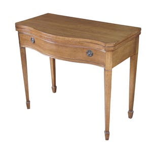 May include: A light brown wooden console table with a curved front and two small drawers. The table has four slender, tapered legs and a smooth, polished surface. The drawer pulls are circular and metallic.