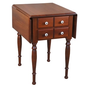 May include: A dark brown wooden drop-leaf table with four drawers and turned legs. The table has a simple design and is perfect for a small space.