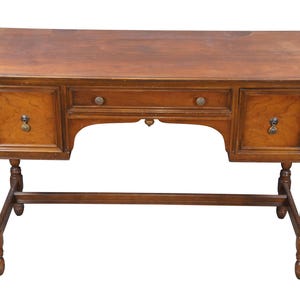 May include: A wooden desk with a warm brown finish. It features two drawers with round knobs and two cabinet doors with decorative pulls. The desk has turned legs and a lower support beam.