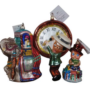 May include: Three glass Christmas ornaments. One is a clock with a man ringing a bell, another is an elephant with a rider, and the last is a child sitting on a pile of presents.