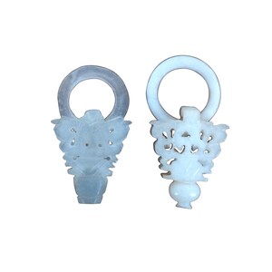 May include: Two carved jade bottle stoppers. One is a pale blue-green color, the other is white. Both have a ring at the top and a decorative floral design. The stoppers are displayed against a white background.