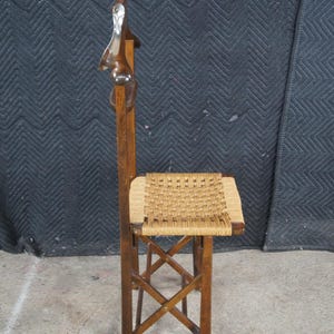 May include: A vintage wooden folding chair with a woven seat. The chair has a tall back with a decorative carved element at the top. The wood has a warm, brown tone, and the seat is a light tan color.
