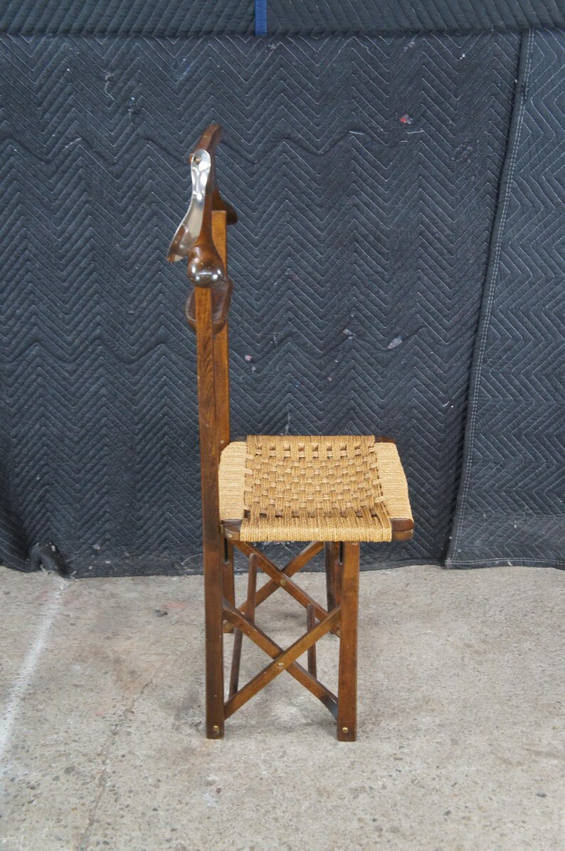 May include: A vintage wooden folding chair with a woven seat. The chair has a tall back with a decorative carved element at the top. The wood has a warm, brown tone, and the seat is a light tan color.