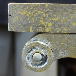 K&ouml;nnte beinhalten: Nahaufnahme eines goldbemalten Holztischbeins mit einem dekorativen Rollendesign. Die Farbe ist abgeplatzt und abgenutzt, wodurch das darunterliegende Holz sichtbar wird.