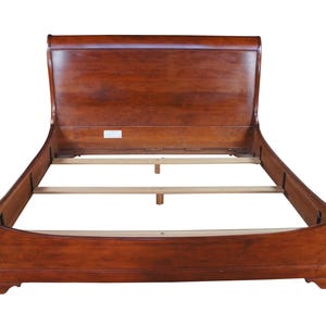 May include: A wooden sleigh bed frame with a rich, dark brown finish. The headboard and footboard have a curved design, and the frame includes wooden slats for supporting a mattress. The bed frame is designed for a standard mattress size.