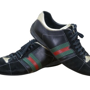 May include: Pair of black sneakers with green and red stripes. The shoes have black laces and a gold accent on the heel. The brand name is visible on the side of the shoe.