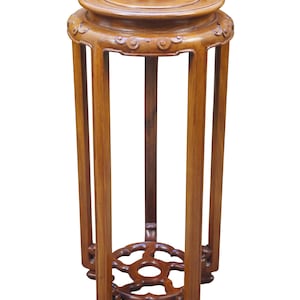 May include: A tall, wooden plant stand with a round top and decorative carved details. The stand has four long, slender legs and a circular base with an openwork design. The wood has a warm, reddish-brown tone.
