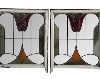 May include: A pair of antique stained glass windows with a tulip design. The windows are framed in white wood and have a distressed look. The glass is multi-colored and features shades of green, red, and orange.