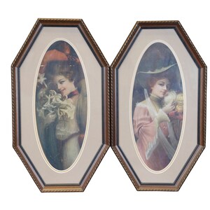 May include: Two framed oval prints of women in vintage clothing. The woman on the left is holding a bouquet of white flowers and the woman on the right is holding a white bird. Both frames are octagonal and have a brown wood finish.