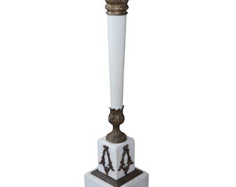 May include: A white marble pedestal table with a square top and a gold-colored base. The base features intricate floral designs and a decorative finial.