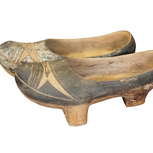 May include: A pair of wooden clogs with black painted designs. The clogs have a high heel and are made of natural wood.