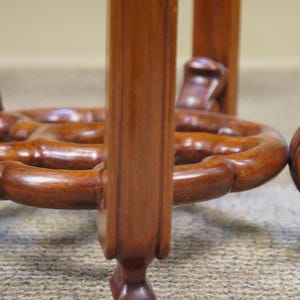 May include: Close-up of a wooden table base with a rich, brown finish. The base features intricately carved details, including a circular design and rounded legs. The wood grain is visible, adding to the table's classic aesthetic.