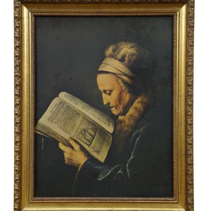 May include: A framed painting depicts a woman reading a book. The woman is wearing a dark coat with a fur collar and a head covering. The painting is in a gold ornate frame.