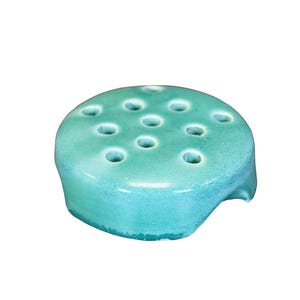 May include: A turquoise ceramic flower frog with multiple holes for arranging flowers.