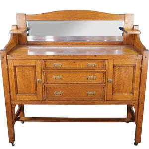 May include: A wooden antique dresser with a mirror, featuring three drawers and two cabinet doors. The dresser is made of light brown wood and has brass hardware. The mirror is rectangular and set into the top of the dresser.