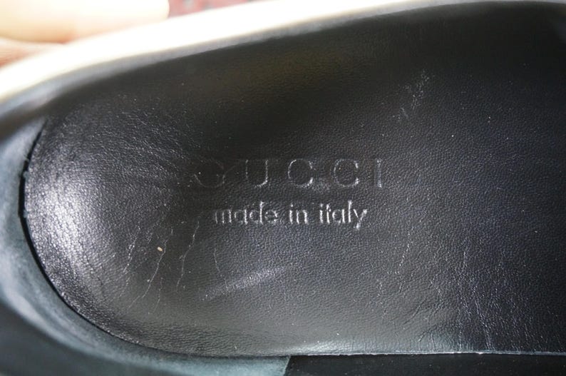 May include: Close-up of the interior sole of a black shoe. The embossed text reads "GUCCI made in italy". The leather sole has a textured appearance.