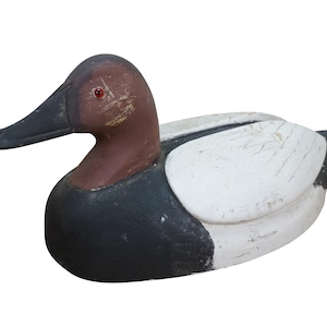 May include: A wooden duck decoy with a brown head, black beak, and red eye. The body is painted black and white, with a distressed finish. This decorative item is a classic piece of Americana.