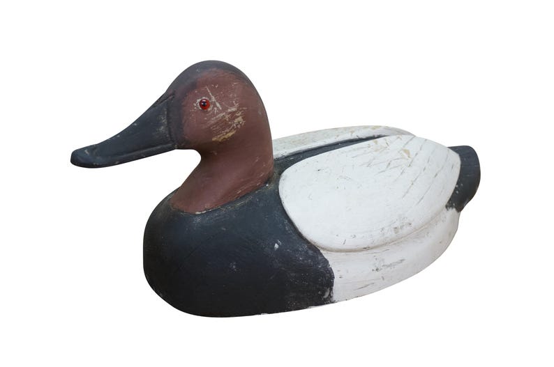 May include: A wooden duck decoy with a brown head, black beak, and red eye. The body is painted black and white, with a distressed finish. This decorative item is a classic piece of Americana.