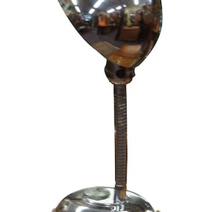 May include: A chrome desk lamp with a round, adjustable shade and a coiled cord. The lamp has a simple, mid-century modern design.