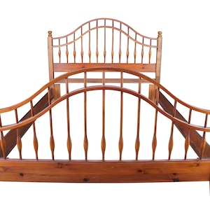 May include: A wooden bed frame with a headboard and footboard. The frame is made of light brown wood and features a curved design with vertical spindles. The headboard has an arched top with vertical spindles. The bed frame is designed for a standard mattress.