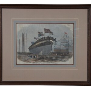 May include: A black and white print of a ship being built in a shipyard. The ship is surrounded by scaffolding and workers. The print is framed in a brown wooden frame.