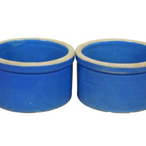 May include: Two cobalt blue ceramic containers with a cylindrical shape and a cream-colored rim. The containers are empty and have a smooth, glossy finish. They are likely for kitchen or home decor.