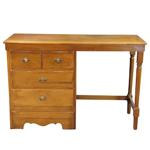 May include: A light brown wooden desk featuring a rectangular top and a single pedestal on the left side. The pedestal contains two small upper drawers and two larger lower drawers, all equipped with small, ornate, metallic drawer pulls.