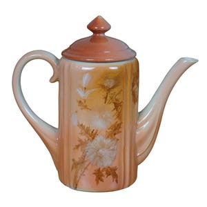 May include: A vintage ceramic teapot with a floral design in shades of orange, brown, and white. The teapot has a lid with a pointed top and a spout on the side.