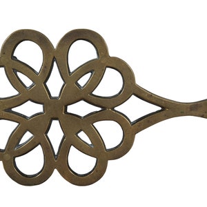 May include: A brass trivet with a decorative, intricate design. The trivet has a long handle with a hole at the end.