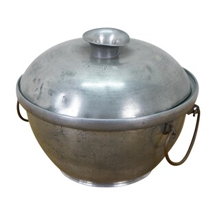 May include: A vintage metal cooking pot with a lid. The pot is a dull silver color with a rounded body and a matching lid. It has two metal handles and a small knob on top of the lid.