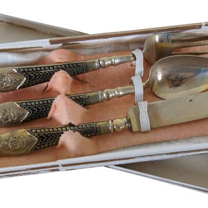 May include: A set of three silver-plated utensils with black and gold handles in a white box. The utensils include a fork, spoon, and knife.