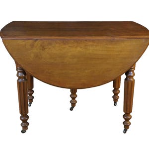 May include: A brown wooden drop-leaf table with a smooth rectangular top and two rounded hinged leaves. The table features four turned legs with vertical fluting details, each supported by a small metal caster wheel at the base for mobility.