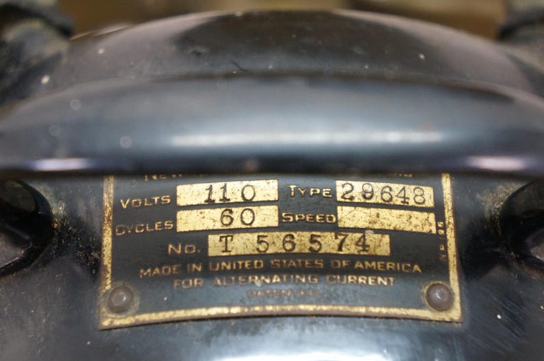 Puede incluir: Primer plano de una placa de motor el&eacute;ctrico antiguo. La placa dorada tiene texto negro que indica 110 voltios, 60 ciclos y el tipo 29648. El texto tambi&eacute;n dice "Made in United States of America for Alternating Current."