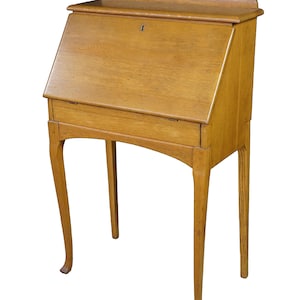 May include: A light brown wooden secretary desk featuring a slanted drop-front lid with a central keyhole, a flat top surface with a raised back edge, and four slender, slightly curved legs that provide a stable base for the rectangular frame.