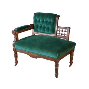 May include: A wooden fainting couch with dark brown legs and frame, featuring a deep green velvet upholstered seat and a tufted backrest. The piece includes one upholstered armrest and a decorative open-work wooden side panel with spindles.