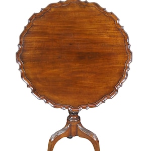 May include: A round, antique wooden table with a scalloped edge. The table has a dark brown finish and sits on a tripod base with carved details. The table's diameter is approximately 30 inches.