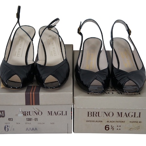 May include: Two pairs of black patent leather peep-toe heeled sandals with slingback straps. The shoes are on their original boxes, which are labeled "Bruno Magli".
