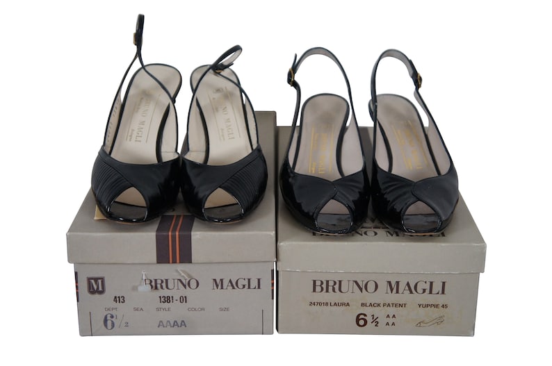 May include: Two pairs of black patent leather peep-toe heeled sandals with slingback straps. The shoes are on their original boxes, which are labeled "Bruno Magli".