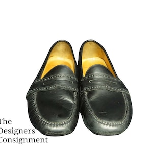 May include: A pair of black leather loafers with a penny strap detail. The loafers have a brown leather lining and a stitched edge.
