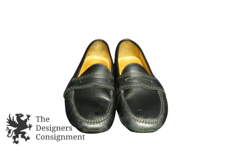 May include: A pair of black leather loafers with a penny strap detail. The loafers have a brown leather lining and a stitched edge.
