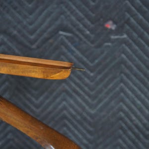 May include: Close-up of a wooden clothes hanger with a dark finish. The hanger has a curved design with a metal hook and a wooden bar for hanging garments. The wood grain is visible.