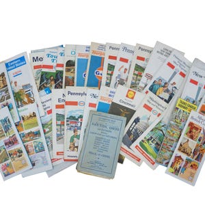 May include: A collection of vintage travel maps and brochures, including state and regional guides. The brochures feature colorful illustrations and text, with titles like "Pennsylvania," "New York," and "Dayton, Ohio."